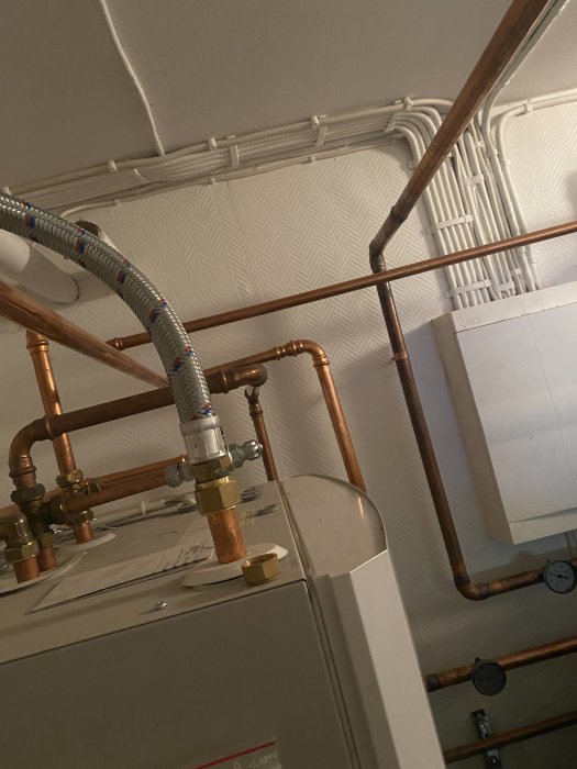 Värmepump med kopplade kopparledningar och cirkulationspump, nederst golvvärmefördelare synlig.