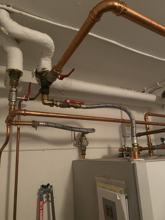 Värmesystem med kopparledningar och cirkulationspump ovanför en värmepump i ett tekniskt utrymme.