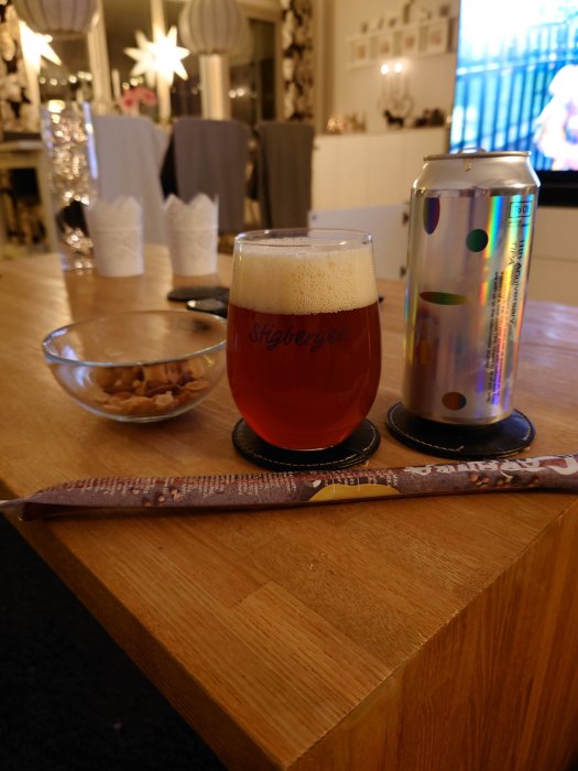 Kvällsmåltid bestående av öl i glas, burk och snacks framför TV i vardagsrum.