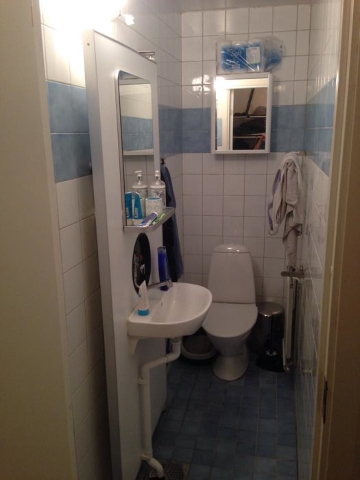 Litet badrum med blått och vitt kakel, spegel, handfat och toalett, liknande användarens eget.