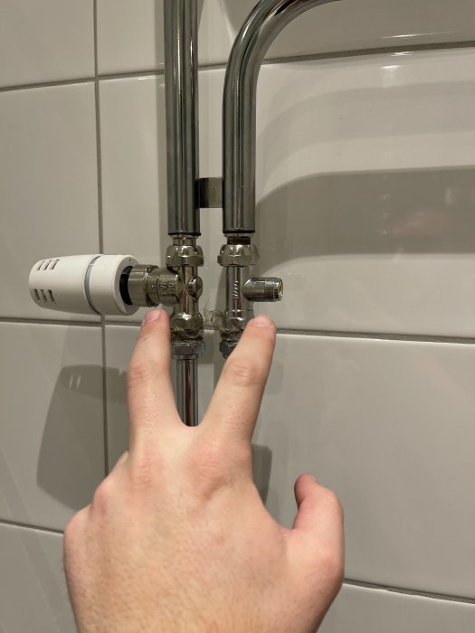 Hand som pekar på rör med termostatkoppling i ett badrum.