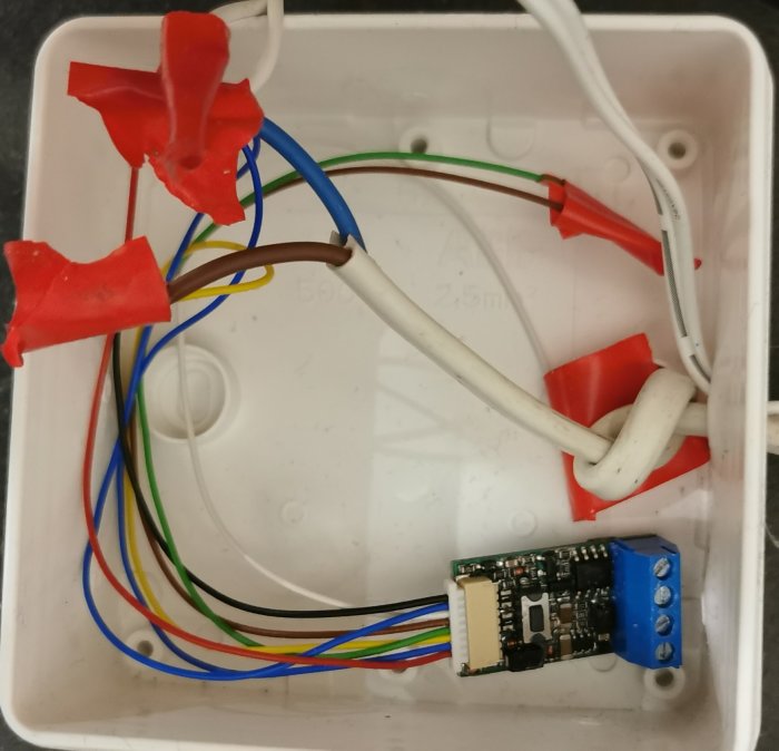 Elektronisk modul i en plastlåda med färgade sladdar kopplade till skruvplintar och isolerade med röd tejp.