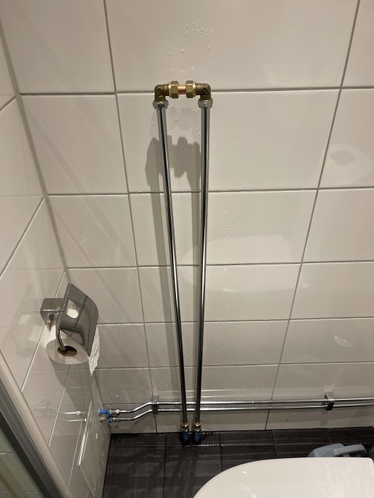 Ett badrum där värmeelement tagits bort, endast rörstumpar kvar på kakelvägg.