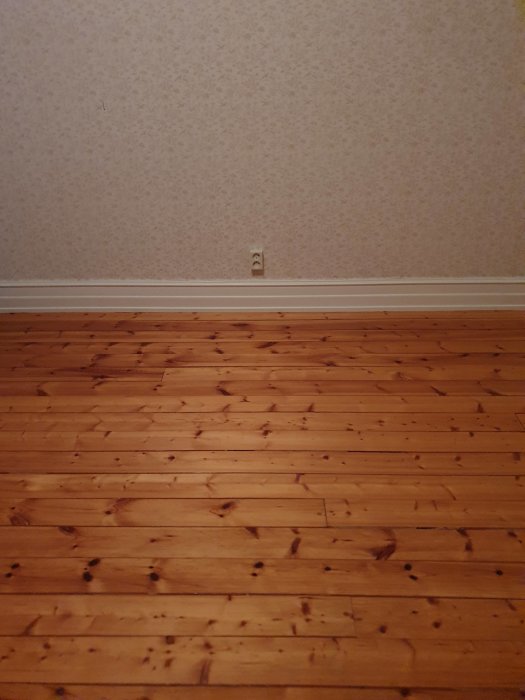 Trägolv med synliga skarvar i ett rum med tjugotalsklassicistisk tapet och golvlister.