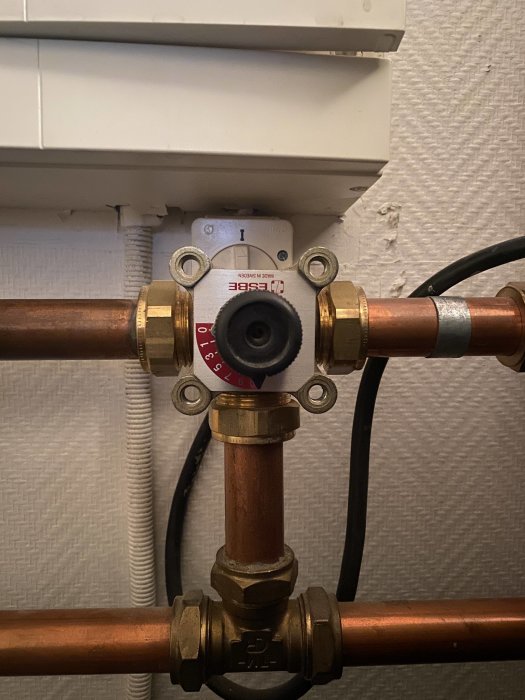 Värmefördelningsventil på kopparrör, placerad under vit rörskyddskanal, fast och ovridbar.