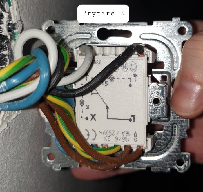 En elektrisk dimmerbrytare öppnad i väggen med synliga trådar och kopplingsschemat på brytarens sida.