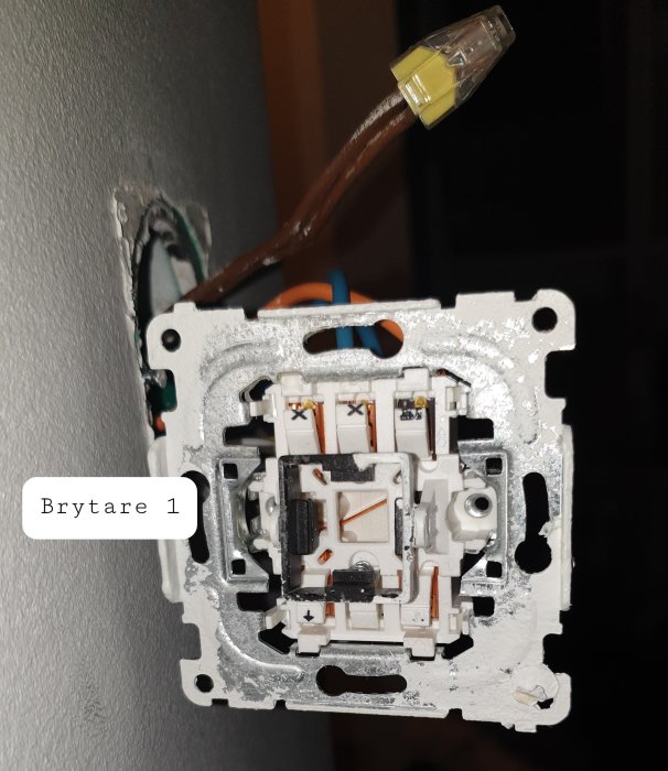 Öppen elektrisk väggbrytare monterad i vägg med synliga kablar och märkning "Brytare 1".