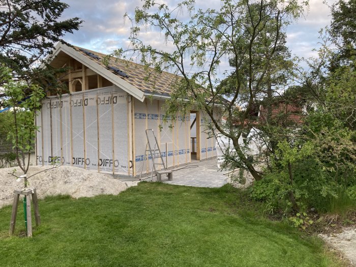 Attefallshus under uppförande med vindduk och utan färdigställda fönster eller ytterpaneler.