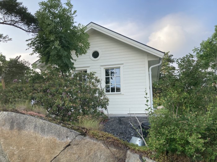 Färdigställd vit ytterfasad på hus med fönster och grönska i förgrunden.