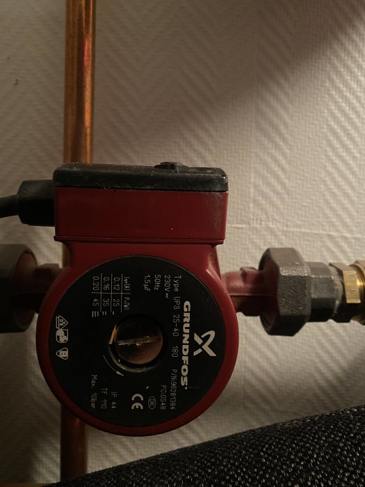 En cirkulationspump för golvvärme ansluten till kopparledningar, med pilfråga.