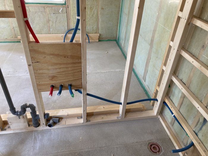 Innervägg i konstruktion med isolering, rördragning och en plywoodskiva.