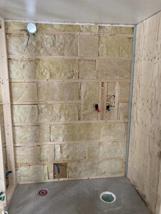 Isolerad vägg med träreglar och mineralull innan innerpaneler monteras i ett byggprojekt.