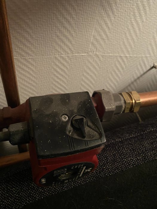 Termostat på en golvvärmefördelare inställd på läge 2 mot en vägg med strukturtapet.