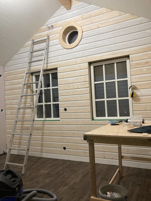 Inredning av hus med träpaneler på väggar, klinkergolv och arbetsverkstad setup, stege vid vägg.