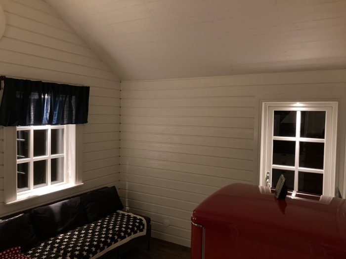 Interiörbild av ett nyrenoverat hörn med soffa, stjärnmönstrad dyna och ett rött kylskåp vid ett fönster.