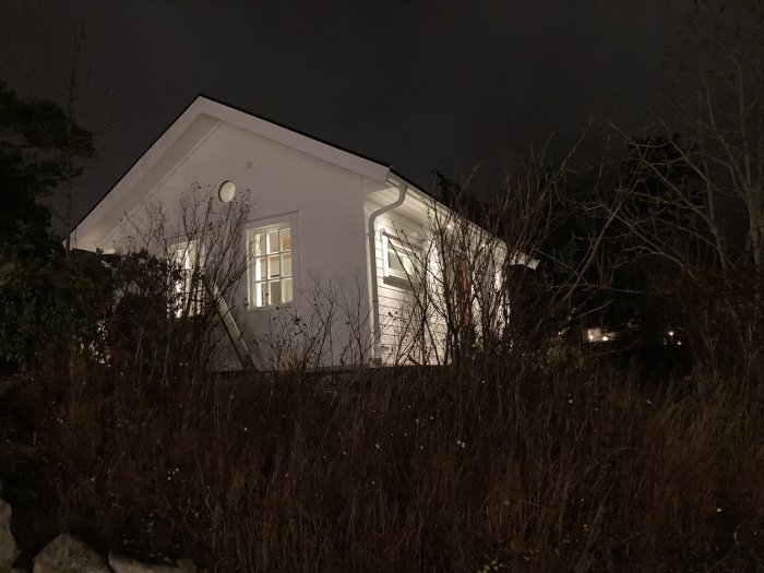Ett nyrenoverat hus belyst på kvällen med synliga fönster och omgivet av vintervegetation.