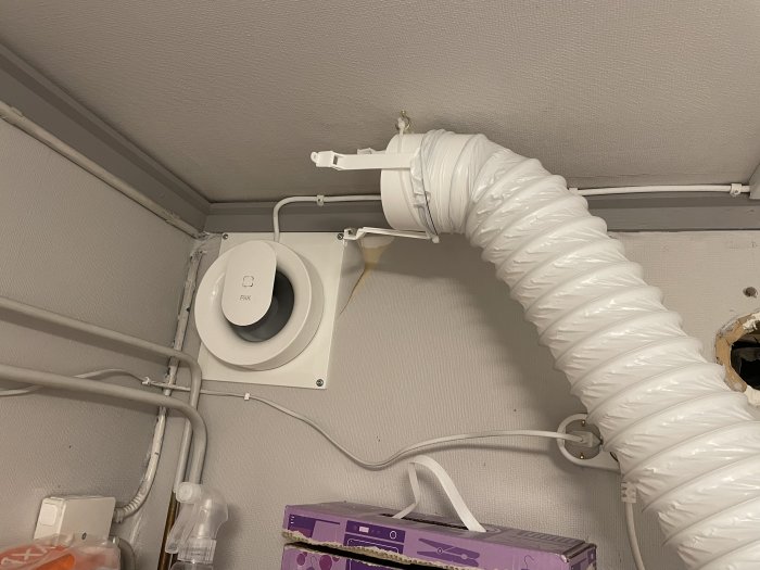 Provisorisk installation av vit köksfläkt med flexibel slang kopplad till ventilation i taket.