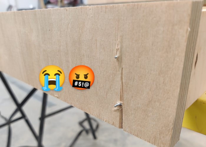 Skiva av spånskiva med spikar inslagna felaktigt vilket orsakat skador, med ledsna och arga emojis överlagt.