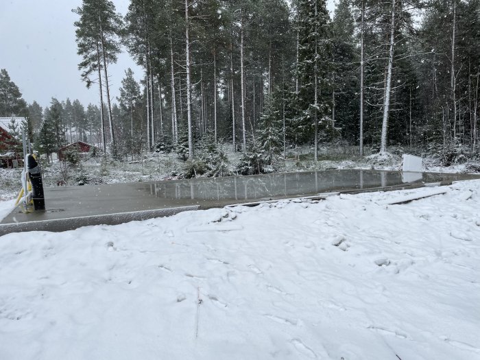 Nyutgjuten betonggrund för garage och hus omgiven av snötäckt mark och skog.