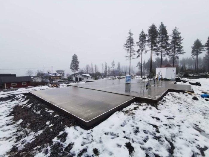 Ny-gjutna betongplattor för garage och hus på ett snötäckt byggarbetsområde.