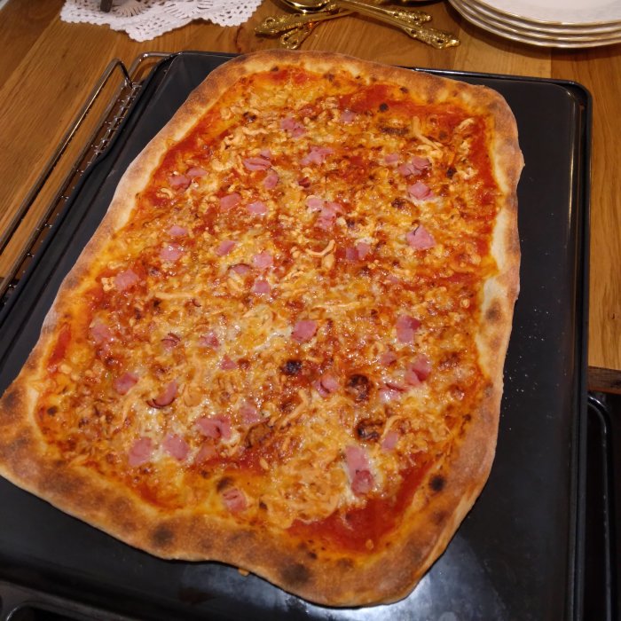 Hemmagjord pizza med välgräddad botten och pålägg av skinka och ost på en bakplåt.