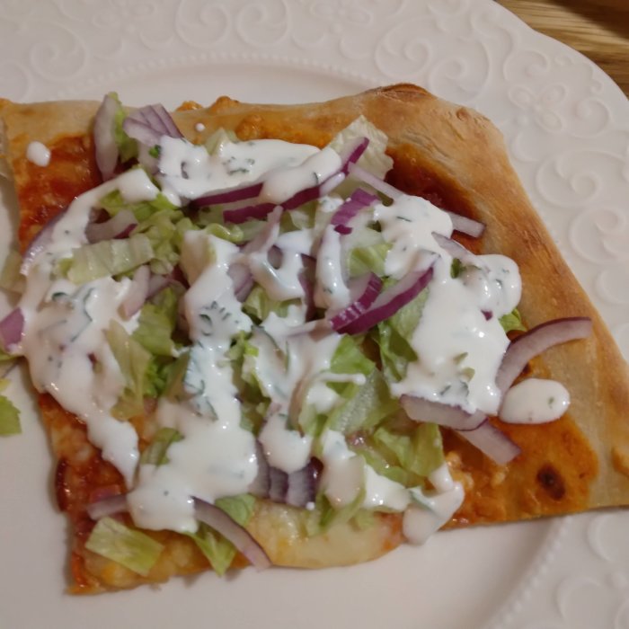 Hembakt pizza med isbergssallad, rödlök och aioli på en vit tallrik.