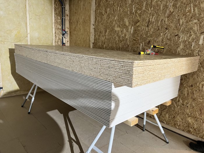 Stapel med isoleringsskivor på skärbord framför en OSB-vägg inne i en byggnad.