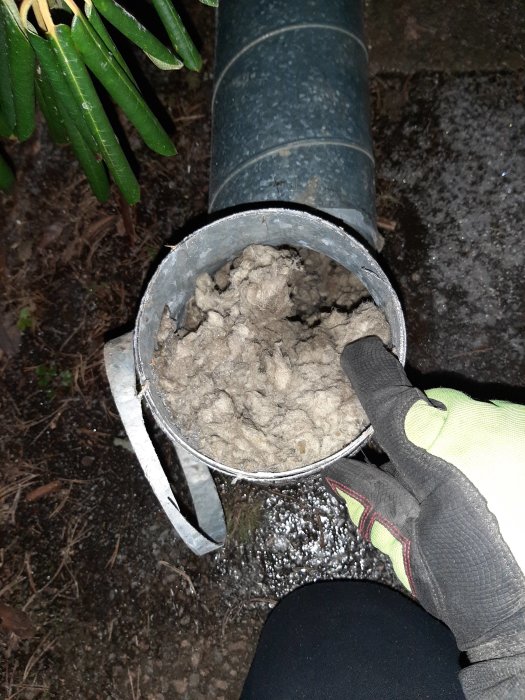 Hand i skyddshandske håller gamla isoleringsmaterial som blockerat ett ventilationsspirorör.