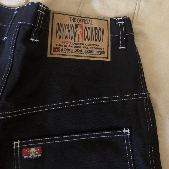 Svarta jeans med etikett texten "THE OFFICIAL PSYCHO COWBOY" och små vita och röda märken på höger sida.