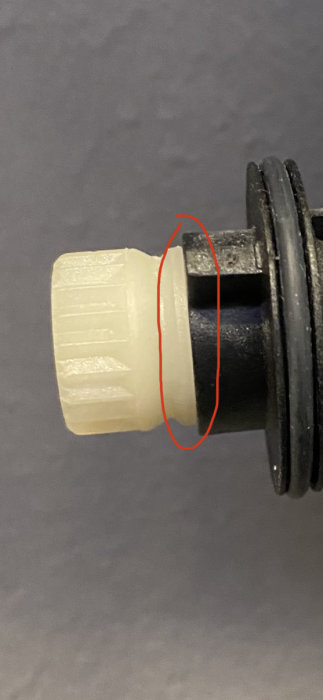 Vit klack på en del skruvas in i en svart del, markerad med röd cirkel som stopppunkt.