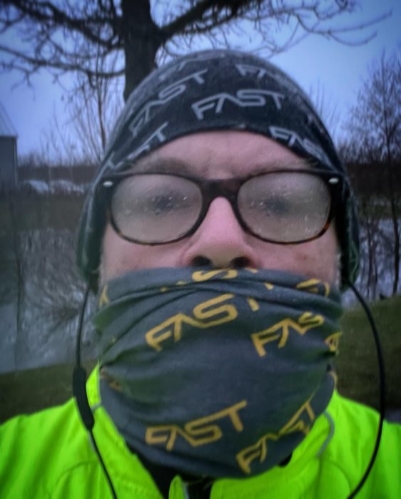 Person med glasögon och munskydd ute i dimmigt väder, bär reflexväst och pannband med texten "FAST".
