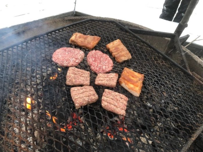 Hamburgare och korv som grillas på utomhusgrill i vinterscen i Brevens bruk.