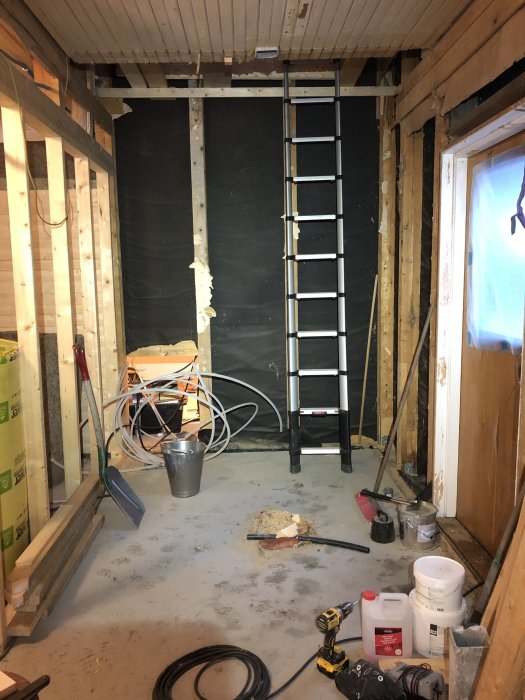 Byggarbetsplats med en temporär stege i ett underkonstruerat trapphus, material och verktyg på golvet.