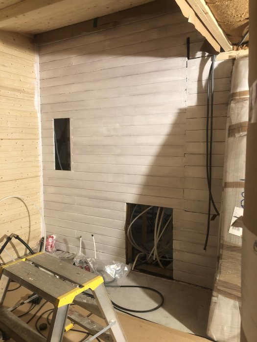 Pågående arbete i ett trapphus med raka och sneda träväggar, stegar och elinstallationer synliga i bakgrunden.
