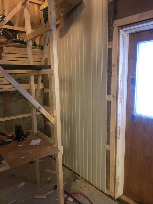 Väggar i trapphus under riktning med synlig träställning, omonterad trappa och byggverktyg.