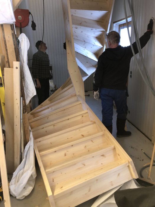 Två män betraktar en nyinstallerad trätrappa i ett trapphus under konstruktion.
