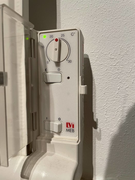 Vit radiator termostat inställd mellan 20-25 grader med synliga kontroller och LOGO MEB.