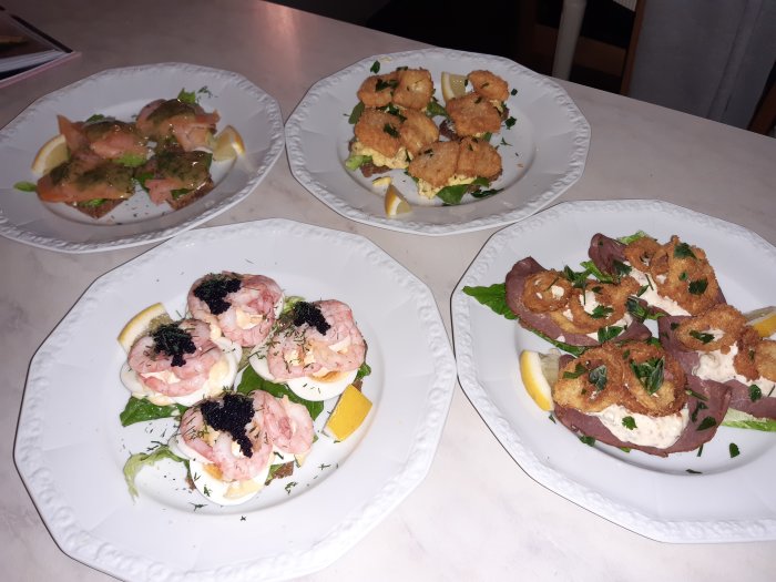 Fyra tallrikar med olika sorter av smørrebrød garnityrade med citron och örter.