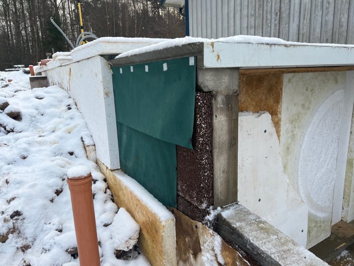 Väggisolering och provisorisk cellplastvägg vid byggprojekt med snötäckt mark.