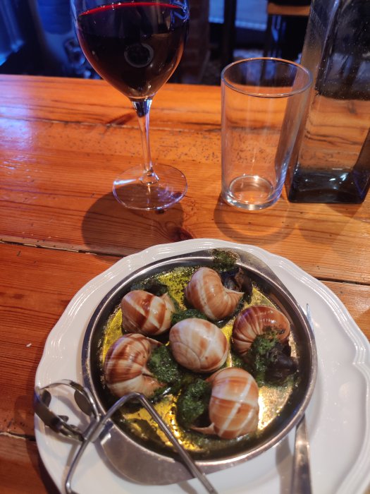 Brunsch med sniglar i vitlökssmör och ett glas rödvin på träbord.