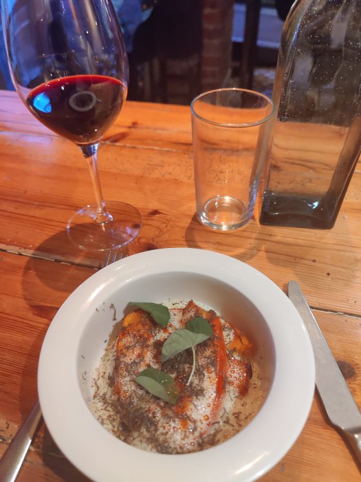 En pumparätt täckt med tryffel i en vit skål, flankerad av ett glas vin och en vattenkaraff på ett träbord.