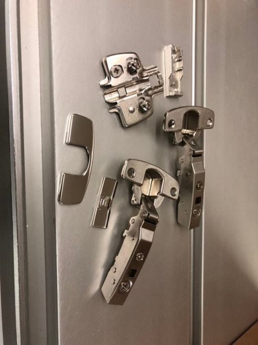 Diverse gångjärnskomponenter från Hettich upplagda på en metallisk yta.