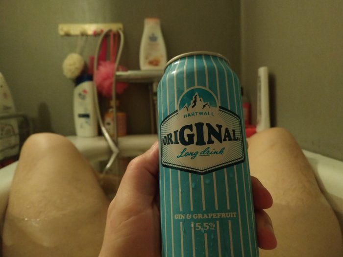 Person som håller en dryckesburk i badkaret med hygienprodukter i bakgrunden.