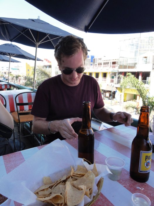 Man med solglasögon äter nachos och dricker öl på en uteservering.