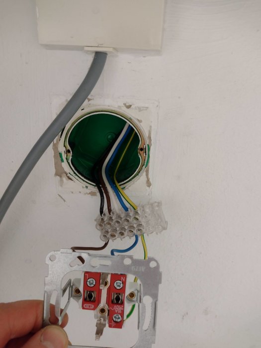 Eluttag utan frontplatta med synliga kablar och ledningar i vägg infästning klar för byte.