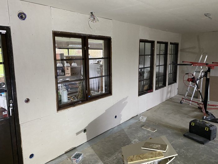 Renoveringsrum med gipsskivor installerade på väggar runt fönster, eluttag och osynlig balk.