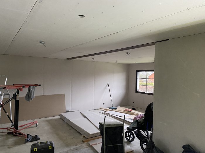 Ett rum under renovering med nästan färdiginstallerade gipsskivor på vägger och i taket, och en synlig balk.