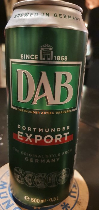 En ölburk DAB Dortmunder Export på ett bord, text "Brewed in Germany" och "Since 1868" synlig.