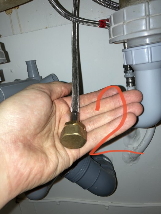 Hand håller ett metallock nära VVS-rör med markerat område A och anslutningar för slangar.