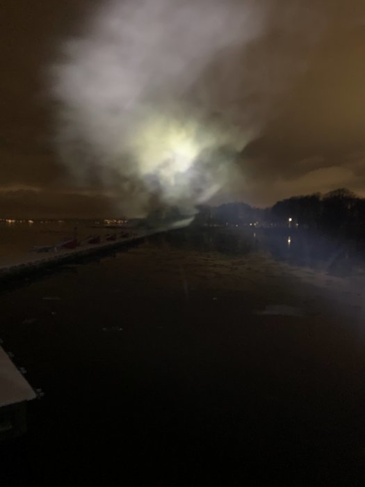 En suddig nattbild av en väg med ljussken och rök, möjligen dimma, över vägytan.